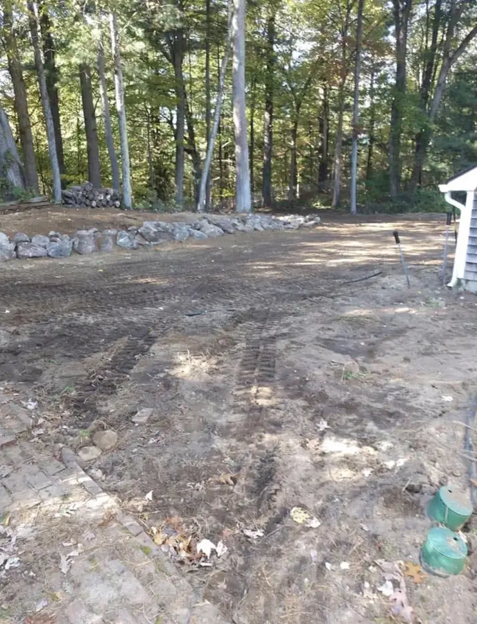 Freshly graded lot with track marks beside a house, E'Bros site prep in Central Massachusetts