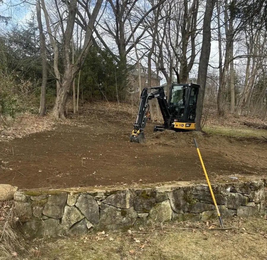 E'Bros mini excavator site grading a yard above a fieldstone wall, Worcester County MA