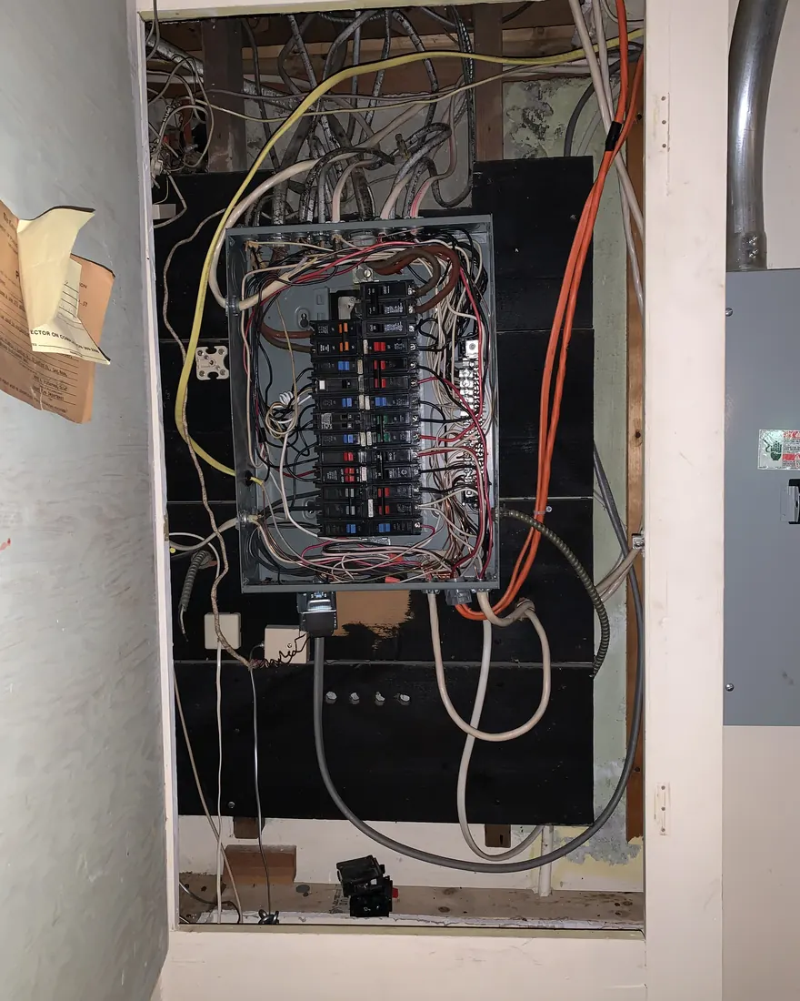 Old fuse panel with tangled cloth insulated wiring in an open wall cavity before replacement by Gourley Electric in Worcester MA