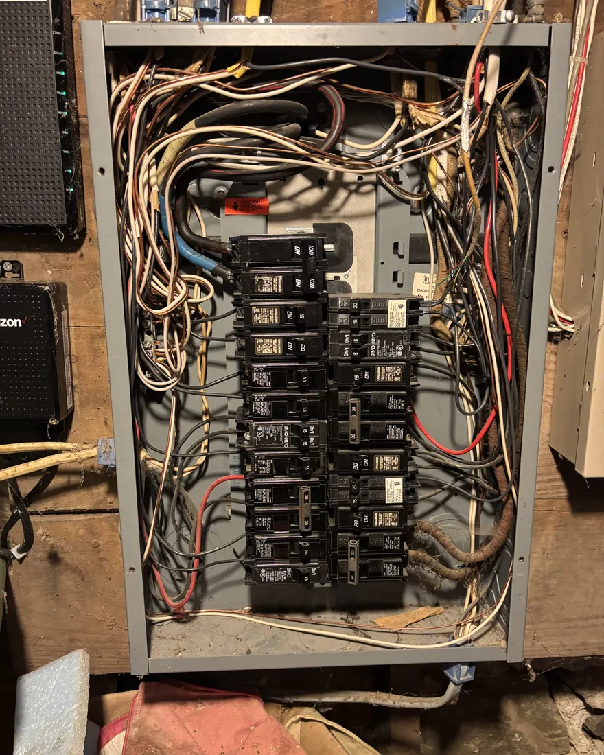 Overcrowded electrical panel packed with tangled loose conductors before rewiring
