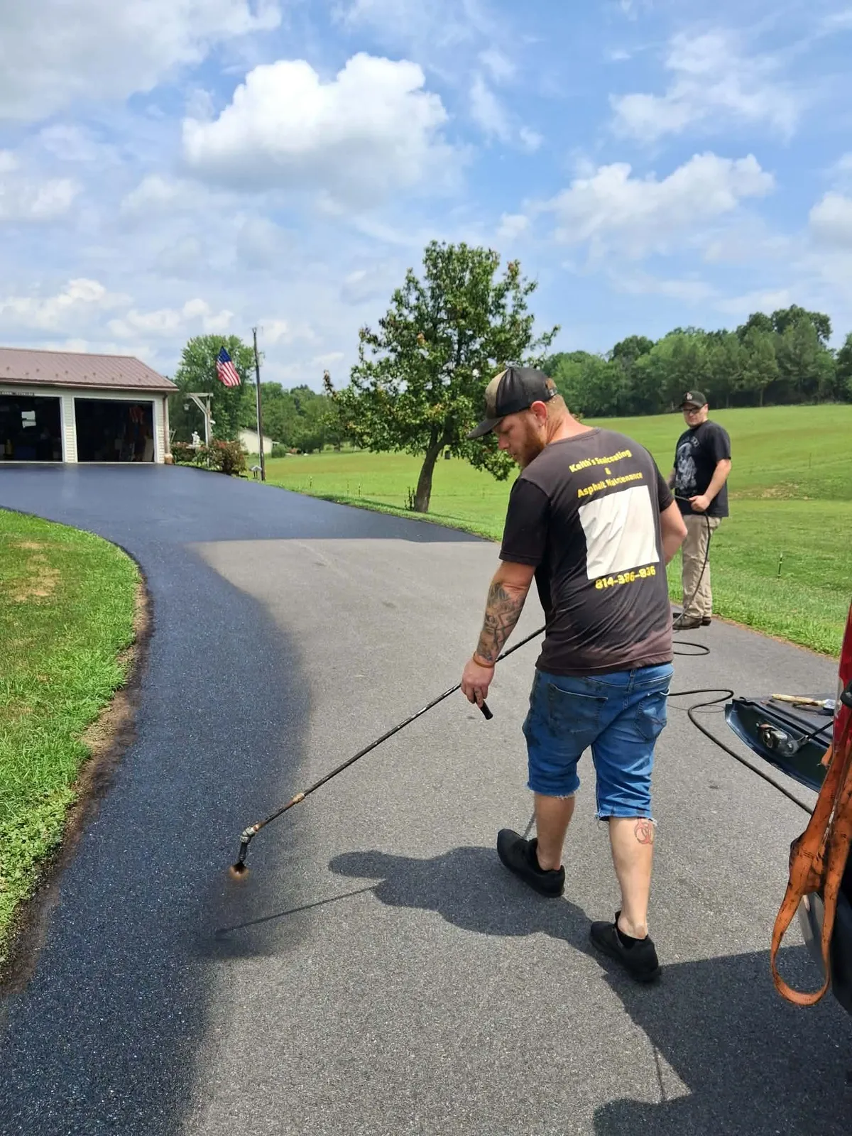 Keith's Sealcoating worker spraying hot tar asphalt sealer onto residential driveway surface