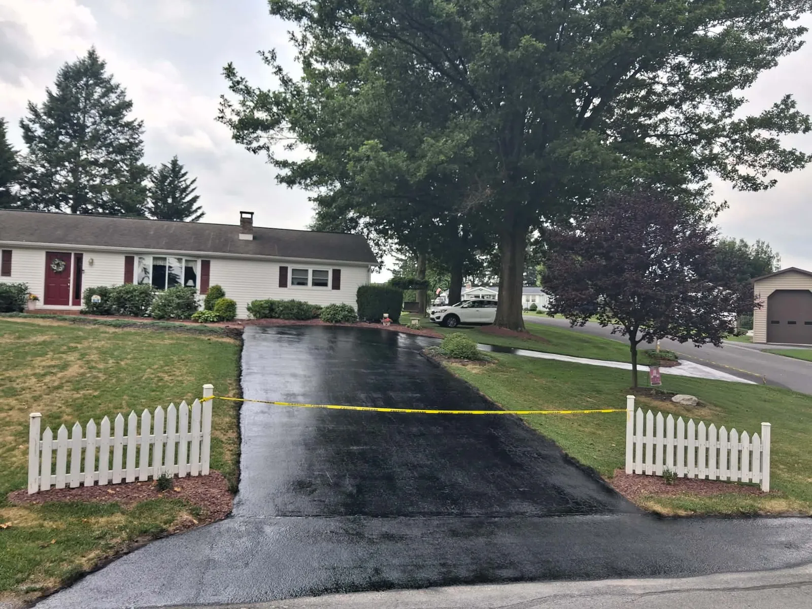Freshly sealcoated residential asphalt driveway showing dark protective gilsonite sealer application
